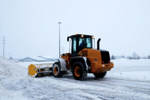 Front end loader works as a snow plow clearing a parking lot during a winter storm.