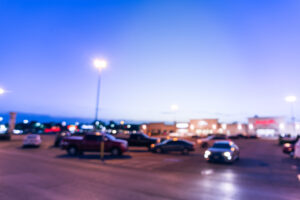 Vintage blurred modern shopping center parking in Texas, USA at blue hour. Exterior mall complex with row of cars in outdoor uncovered parking lots, bokeh of retail store, light poles in background